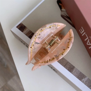 Détail d'une pince à cheveux en acétate rose marbré avec strass et accents dorés