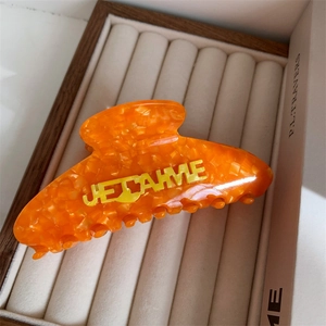 Close-up of bright orange acetate hair claw clip with 3D yellow Je t'aime lettering
