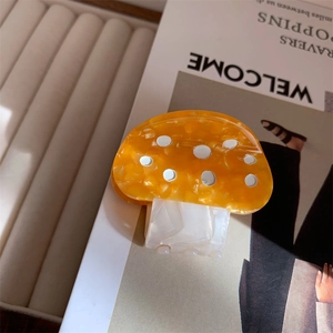 Detail of colorful mushroom hair claw clip with orange white dots on marble acetate