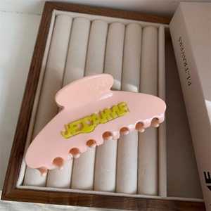 Close-up of pink acetate hair claw with yellow JE T'AIME lettering on velvet display