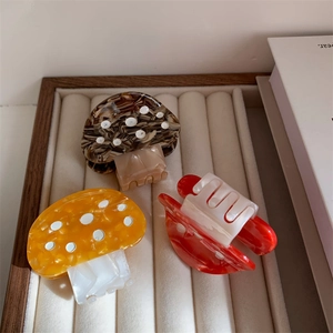 Close-up of three colorful mushroom hair claws with white polka dots on a beige tray