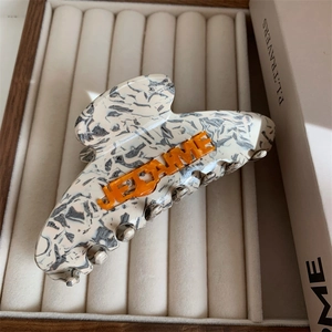 Detail of marble pattern hair claw clip with orange JE T'AIME lettering on white velvet