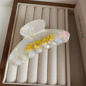 Close-up of white acetate hair claw with yellow JE T'AIME lettering in a jewelry box