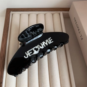 Macro shot of black glossy hair claw featuring 3D white JE T'AIME lettering detail