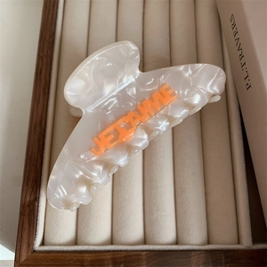 Close-up of cream acetate hair claw with orange JE T'AIME lettering in a velvet jewelry box