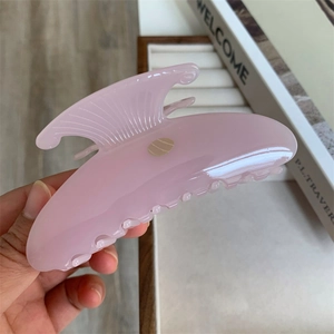 Gros plan d'une pince à cheveux sirène en acétate rose tenue à la main, style vintage