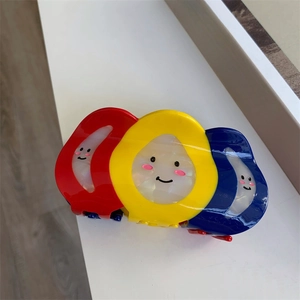 Vue détaillée de grandes pinces à cheveux colorées rouge, jaune et bleu avec smileys