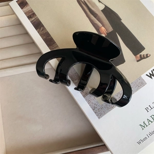 Close-up of glossy black acetate hair claw clip with golden lettering on high-quality magazine