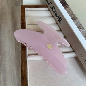 Détail du grand clip à cheveux rose en acétate avec étiquette dorée sur écrin beige