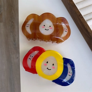 Détail de pinces à cheveux en acétate coloré avec sourires ludiques sur plateau bois