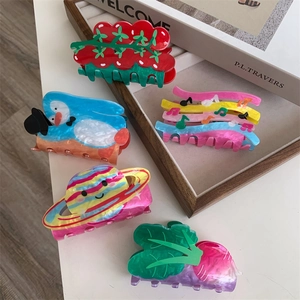 Close-up of creative acrylic hair claws in shapes of notes, planets, and vegetables