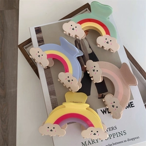 Détail de pinces à cheveux arc-en-ciel avec des nuages souriants posés sur un livre