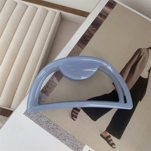 Detail of a Morandi blue acetate hair claw clip with golden letter on a display tray