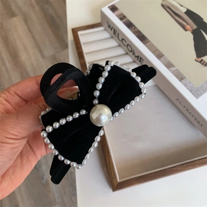 Detail of a black velvet bow hair claw clip with elegant pearl edges and center bead