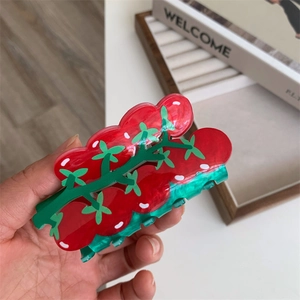 Close-up of creative red tomato hair claw clip with green leaf detail and acrylic finish