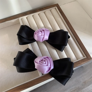 Close-up of elegant black silk ribbon bows with purple satin roses in a 2-piece hair clip set