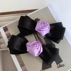 Detailed view of two black satin bow hair clips with delicate purple silk roses