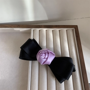 Detail of a black satin ribbon bow hair clip with a small lilac handmade rose flower