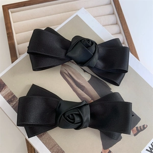 Close-up of two black satin bow hair clips with delicate handmade rose floral centers