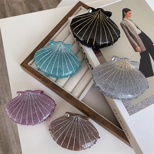 Five colorful shell-shaped hair claws with rhinestones and glitter finish on a tray