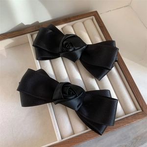 Close-up of black satin bow hair clips with handmade roses in a beige jewelry box
