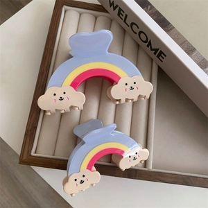 Détail de pinces à cheveux arc-en-ciel colorées avec nuages souriants et finition résine