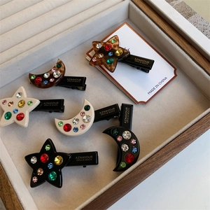 Détail des barrettes lune et étoile ornées de strass colorés sur un plateau blanc
