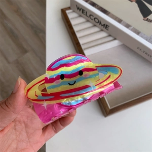 Colorful rainbow planet acrylic hair claw clip with smiling face shown in a hand