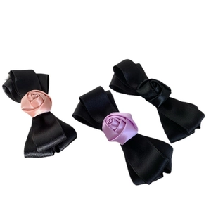 Three handmade satin bow hair clips with rose accents in pink, purple, and black colors