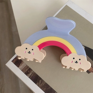 Détail d'une pince à cheveux arc-en-ciel avec nuages souriants et finition pailletée