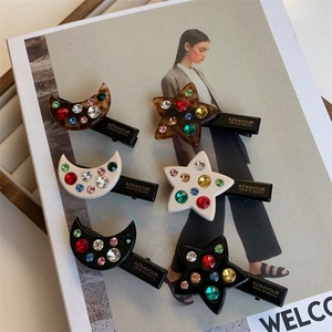 Détail de six barrettes étoile et lune serties de strass colorés sur un magazine de mode
