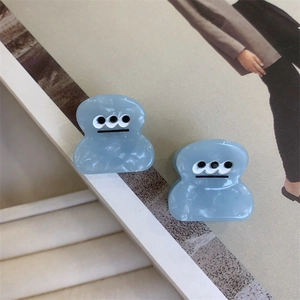 Close-up of blue acetate hair clips with three-eyed cartoon design and marble texture