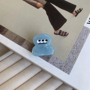 Detail of light blue acetate monster hair claw with cartoon three-eye pattern on magazine