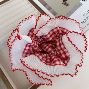 Detailed view of red plaid scrunchie with white lace trim on a white display tray