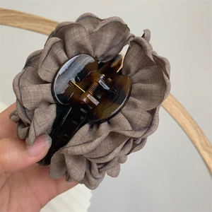 Detail of large brown pleated fabric hair claw clip with shell pattern plastic texture