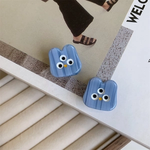 Detail showing blue acetate hair claw with funny three-eyed monster design and stripe texture