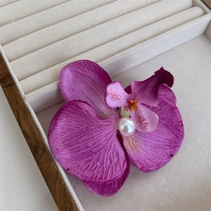 Detail of purple orchid hair clip with white pearl center on a beige velvet jewelry tray