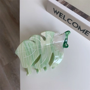 Gros plan détaillé d'une pince à cheveux en acétate motif feuille de monstera vert marbré
