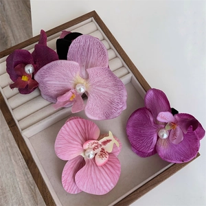 Detail of four faux orchid hair clips with white pearls in a wooden jewelry tray