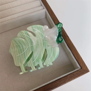 Détail d'une pince à cheveux feuille de monstera en acétate marbré vert et blanc
