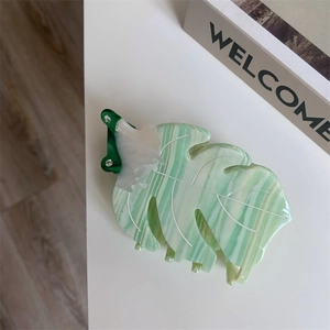 Gros plan d'une pince à cheveux feuille de monstera au fini marbré vert et strass