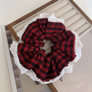 Close-up of red plaid scrunchie with white floral lace trim on a velvet display tray