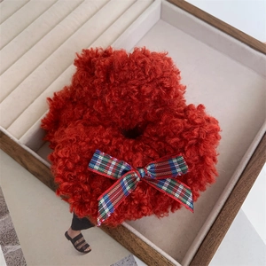 Red plush scrunchie with plaid bow accent displayed in a warm jewelry tray setting