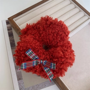Close-up of red teddy fleece scrunchie with a plaid bow on a beige jewelry tray