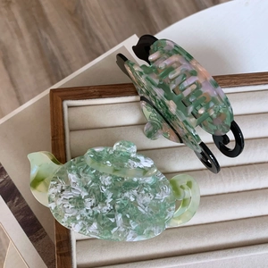 Detail view of teapot-shaped hair claw made of green marble texture acetate material