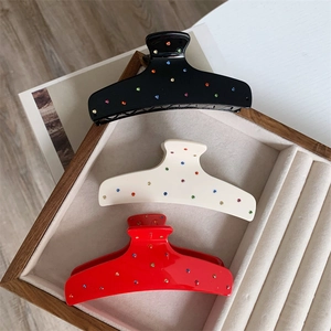 Three-piece rhinestone claw clip set in black, cream, and red on a wooden tray