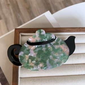 Unique teapot hair claw clip with marble green and pink acetate design in a display tray