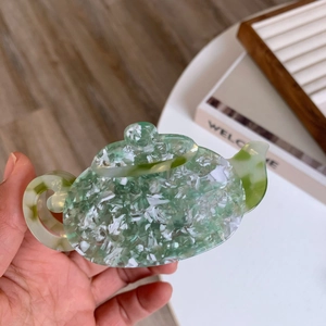 Detail of teapot-shaped hair claw clip made of marble-textured green acetate