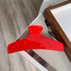 Macro view of a red curved claw clip decorated with colorful rhinestones on a wooden base