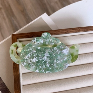 Detailed view of teapot shaped acetate hair claw clip with green marble texture